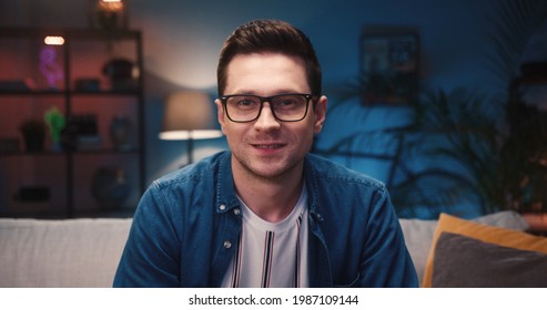 Close Up Of Caucasian Young Handsome Guy In Glasses Watching Television Choosing Channel While Sitting On Sofa And Drinking Beer From Bottle. Man Watch Movie On TV Sitting On Couch At Home, Leisure