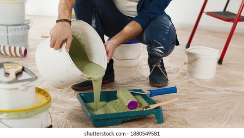 Close up of Caucasian young handsome man pouring green olive paint preparing for painting walls in house renovating and redesigning room. Handyman working on apartment redecoration repair and makeover