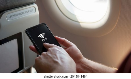 Close Up Caucasian's Hand Holding Smart Phone Sitting By The Airplane Window Tap On The Screen With Wi-fi Onboard Signal. Internet Wifi Service During The Flight, Flight Mode Internet Service Concept.