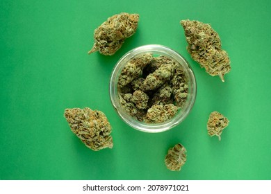 Close up of cbd cannabis buds in glass jar, macro view. Medicinal marijuana blooms on green paper background. Hemp drying flowers, top view.