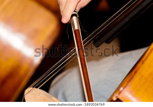 Close up of a cello player. You can see the hand,\
the bow and the strings