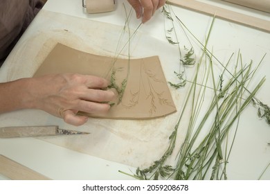 Close up ceramist hands imprinting herb on raw clay with rolling pin. Handmade, hobby art and handicraft concept. - Shutterstock ID 2059208678