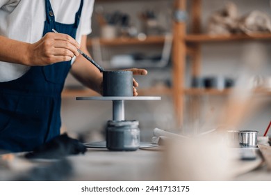 Close up of ceramist's hands making clay mug at ceramics studio. Cropped picture of craftswoman's hands using pottery tool and making handmade earthenware at pottery workshop. Manufacturing concept. - Powered by Shutterstock