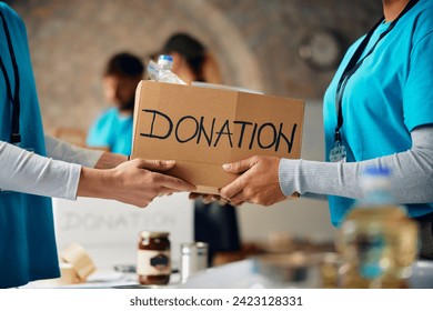 Close up of charity workers cooperating while packing donation boxes at food bank. 
