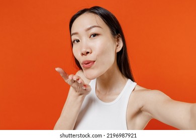 Close Up Charming Fun Young Woman Of Asian Ethnicity 20s Years Old In White Tank Top Doing Selfie Shot Pov On Mobile Phone Blowing Sending Air Kiss Isolated On Plain Orange Background Studio Portrait