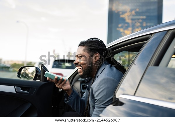 Close
up cheerful african businessman talking on mobile phone in new car.
Smiling African American man sitting in a luxury car. Cheerful
african businessman having a phone call in the
car.