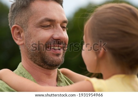 Close up of cheerful dad looking at his little girl, holding her while spending time together outdoors on a warm day