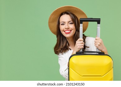 Close up cheerful fun traveler tourist woman in casual clothes hat hiding with yellow suitcase valise isolated on green background Passenger travel abroad weekends getaway Air flight journey concept.