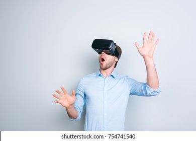 Close up of cheerful student in shirt wearing virtual reality goggles, getting experience using VR-headset of virtual reality, gesticulating, touching something with his  hands in gray background - Powered by Shutterstock