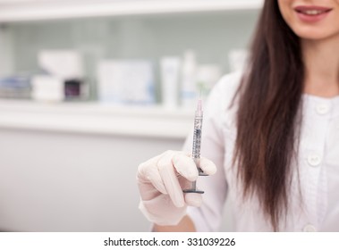 Close up of cheerful young cosmetologist holding squirt for botox injection.  woman is standing in her office and smiling. Copy space in left side