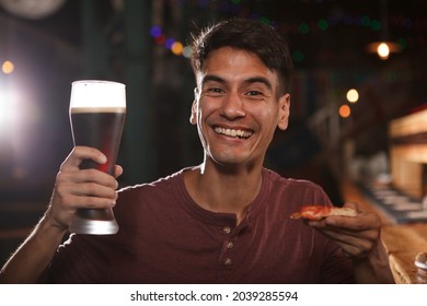 Close Up Of A Cheerful Young Man Holding Beer Glass And Pizza Slice, Smiling To The Camera