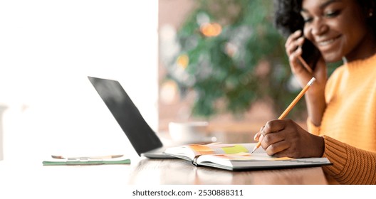 Close up of cheery black lady taking notes while having phone conversation at cafe, looking for job, free space - Powered by Shutterstock