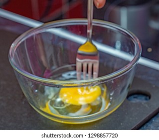Close up of a chef about to beat an egg and egg yolk with a stainless steel fork in a glass pyrex bowl
