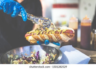 Close up of chef hands adding vegetables on fresh hot dog with grilled sausage. - Powered by Shutterstock