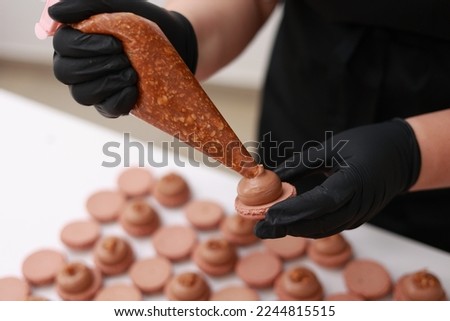 Close up of chef hands putting salt caramel with nuts in ganache cream on chocolate macarons shells. Macaroon Baking Concept. Cooking, Food And Baking Concept. Confectionery And Baking Concept