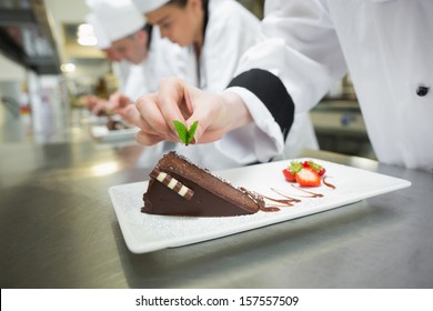 Gros plan sur un chef mettant une feuille de menthe sur un gâteau au chocolat dans une cuisine occupée : photo de stock