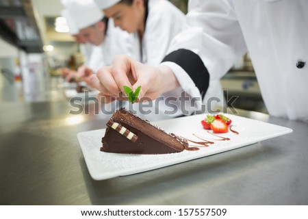 Close up of chef putting mint leaf on chocolate cake in busy kitchen