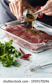 Close Up Of A Chef's Hands Pouring Marinade On A Flank Of Raw Beef.