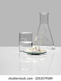 Close up chemical ingredient on white laboratory table. Calcium carbonate Chip in Chemical Watch Glass place next to beaker with alcohol and Erlenmeyer flask. Side View