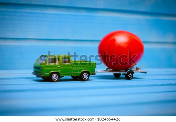 Close up of chicken\
egg on toy car with a trailer on a blue wooden background. Abstract\
retro concept\
