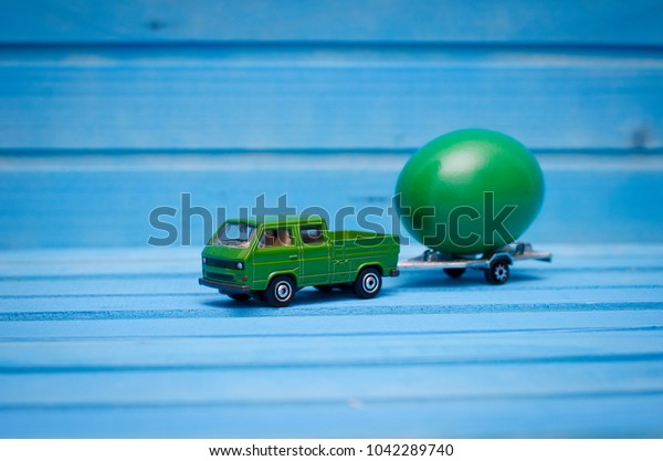 Close up of chicken
egg on toy car with a trailer on a blue wooden background. Abstract
retro concept
