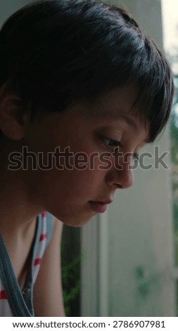 Close up of child face by window with downcast gaze highlighting introspection, solitude, vulnerability and pensive mood indoors