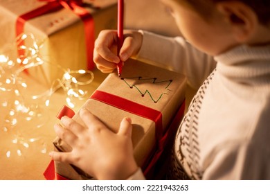 Close up child hand paints gift box New year present packaging. Making surprise for family. Dream. Children's paper craft school kindergarten. Christmas eve holiday party lights and ringing bells. - Powered by Shutterstock