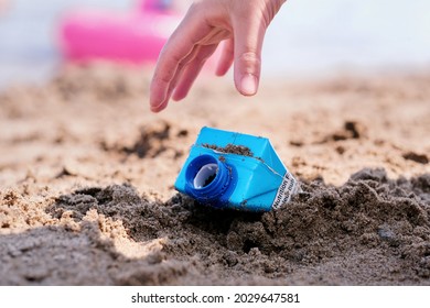 Close up of child hand picking up 
empty drink carton recycle garbage from sandy beach. Environment protection, garbage recycle and environmental awareness concept. - Powered by Shutterstock