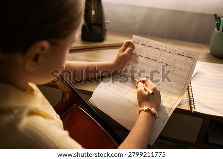 Close up of child studying music notation and practicing string instrument at desk, developing creative skills and discipline. Useful for music education, lessons, youth learning