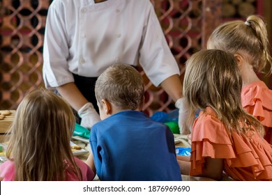 Close Up Of Children Decorating Christmas Biscuits And Gingerbread Cookies In Kitchen Together With Chef. Kids Cooking Class. Merry Christmas And Happy Holidays Concept