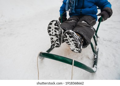 Close up of child's feet in boots covered with snow. Child is sitting on sled. - Powered by Shutterstock