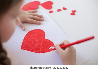 Close up child's hands drawing a red heart on a light background. Copy space for text