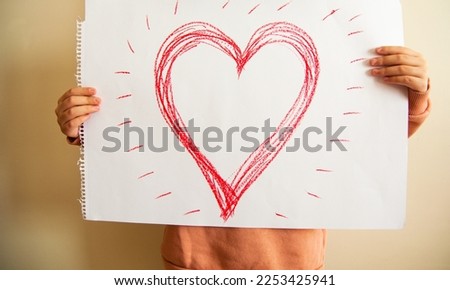Close up of child's hands holding a piece of paper with drawing red heart.