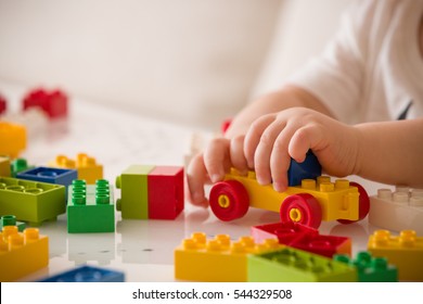 Close up of child's hands playing with colorful plastic bricks at the table. Toddler having fun and building out of bright constructor bricks. Early learning.  stripe background. Developing toys