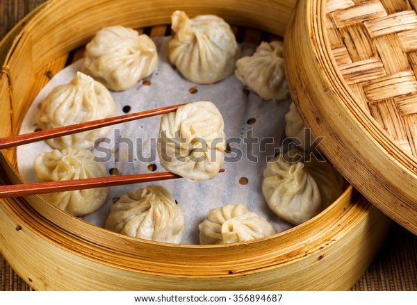 Close up of Chinese steamed dumplings,\
selective focus on piece held in chopsticks, being taken out of\
bamboo steamer with rustic wood in background.  \
