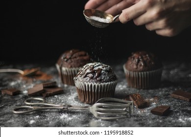 Close Up Of Chocolate Muffins With Icing And Hands Decorating Them With Sugar, Atmospheric Dark Still Life