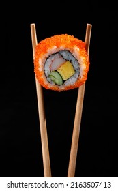 Close Up Chopstick Holding California Maki Sushi Or California Rolls Or Masago Maki Sushi Roll Isolated On Black Background.