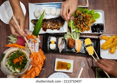 Close up chopsticks to hold fresh salmon sliced for sushi menu.A set of sushi on a wooden table in a Japanese restaurant.Party of friends or family eating sushi using bamboo sticks.