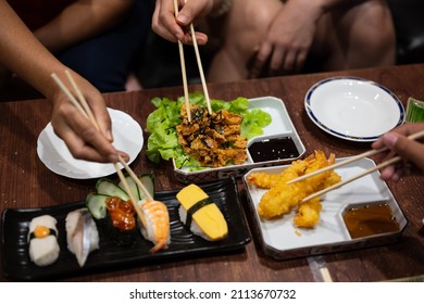 Close up chopsticks to hold sushi roll.A set of sushi on a wooden table in a Japanese restaurant.Party of friends or family eating sushi using bamboo sticks.