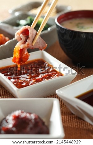 Close up Chopsticks picked pork dipped into white dipping  spicy Sauce bowls on orange placemat.