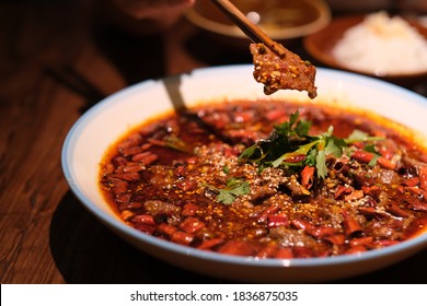 close up chopsticks picking up poached sliced beef in hot chili oil on dinner table. Famous Sichuan cuisine