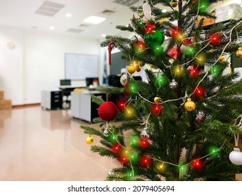 Close Up Christmas Tree In Office Background. Xmas Celebration In Office. Detail Of Christmas Balls And Lights With Working Office.