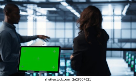 Close up of chroma key tablet next to server room data scientists conducting security audits, preventing bugs. Green screen device and man working with colleague in data center, camera B