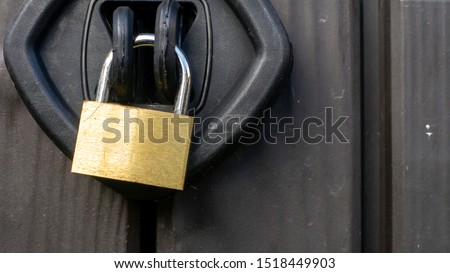 Close up of a chrome and gold textured padlock locking a plastic outside storage unit. Image taken on an overcast day.