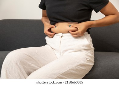 Close Up Of Chubby Woman Holding Her Belly Sit On The Sofa. Diet Lifestyle To Reduce Fat Concept.