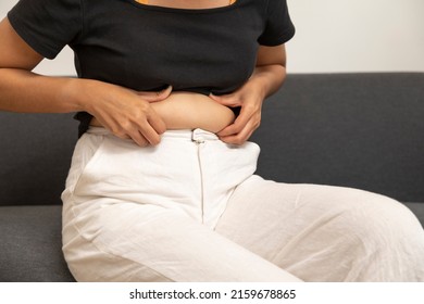 Close Up Of Chubby Woman Holding Her Belly Sit On The Sofa. Diet Lifestyle To Reduce Fat Concept.