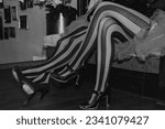 Close up of circus performers women legs in striped red-black stockings, sitting in dressing room. Black white photo of theatrical ladies legs. Theatre performance concept. Copy ad text space banner
