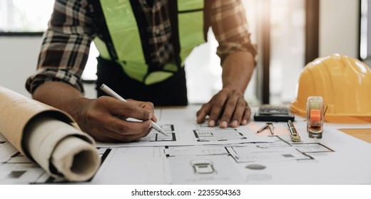 Close up of civil male engineer asian working on blueprint architectural project at construction site at desk in office.