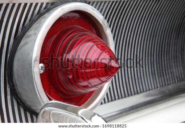 Close up of a\
classic car rear light cluster, including the brake light and\
heavily chromed grill. The vintage car is painted in white coloured\
paint with plenty of\
chrome.