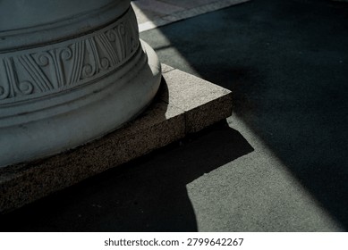 A close up of a classical architectural column base resting on a granite plinth with strong geometric shadows symbolizing stability and design heritage